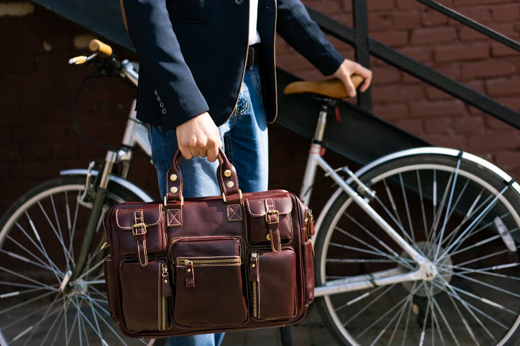 Portrait of a man in a suit holding a leather briefcase next to a bicycle outdoors.