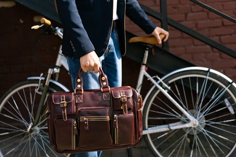 Portrait of a man in a suit holding a leather briefcase next to a bicycle outdoors.
